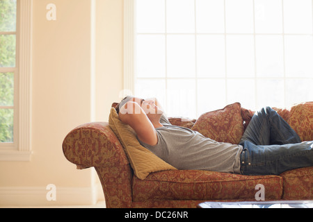 Giovane uomo sdraiato sul divano con le mani dietro la testa Foto Stock