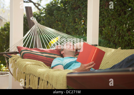 Giovane uomo libro lettura in amaca, ridendo Foto Stock