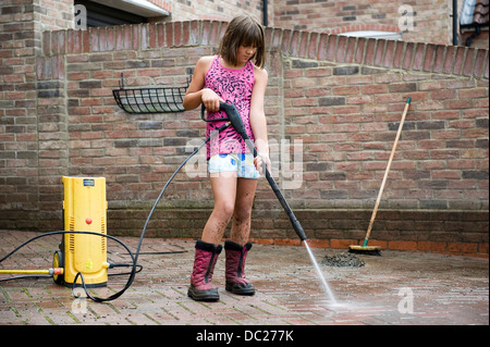 Una ragazza di età compresa tra i 10 utilizza una rondella di potenza per pulire il blocco famiglia pave drive drive a casa sua per pocket money. Foto Stock