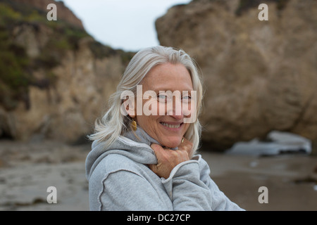 Donna matura che indossa un maglione grigio sulla spiaggia, sorridente