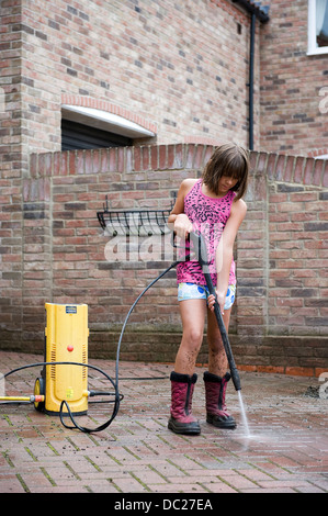 Una ragazza di età compresa tra i 10 utilizza una rondella di potenza per pulire il blocco famiglia pave drive drive a casa sua per pocket money. Foto Stock