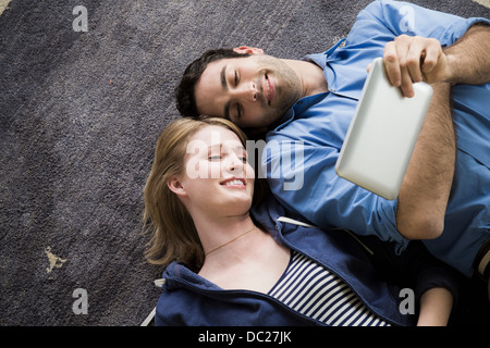 Coppia giovane sdraiato sul pavimento con libro elettronico Foto Stock