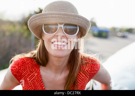 Donna matura indossando occhiali da sole e cappello sorridente verso la telecamera Foto Stock