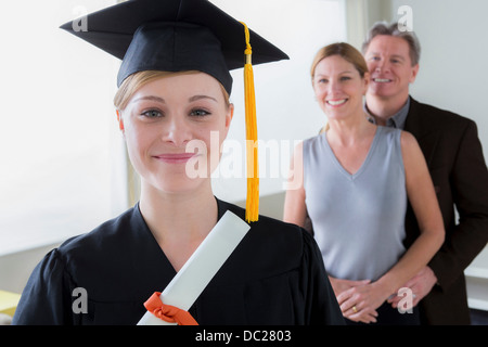 Ragazza adolescente indossando mortarboard con i genitori in background Foto Stock