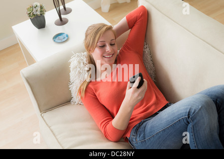 Ragazza adolescente sul divano con un telefono cellulare, sorridente Foto Stock