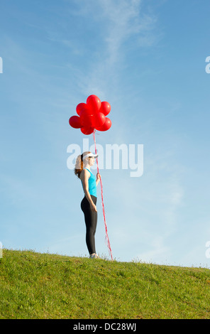 Ragazza adolescente in piedi sull'erba azienda palloncini rossi Foto Stock