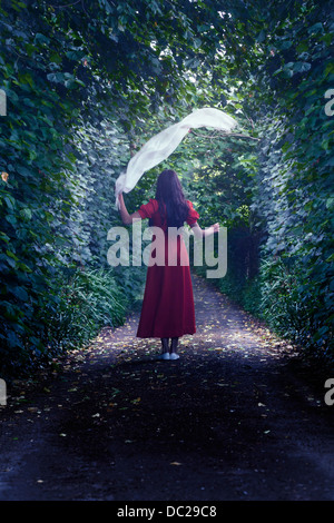 Una ragazza in un abito rosso è a piedi attraverso i boschi con uno scialle bianco Foto Stock