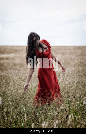 Una ragazza in un abito rosso su un campo, giocando con la granella Foto Stock