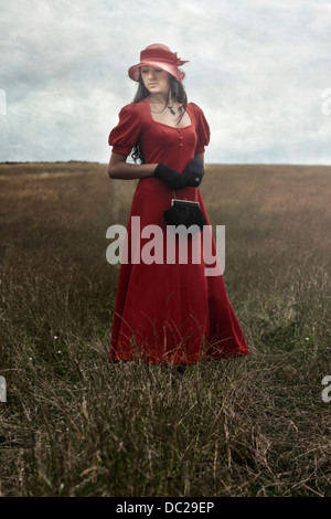Una ragazza in un abito rosso è in piedi su un campo Foto Stock