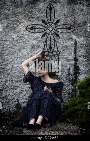 Un dolore di donna con velo e abito scuro seduto su una tomba Foto Stock