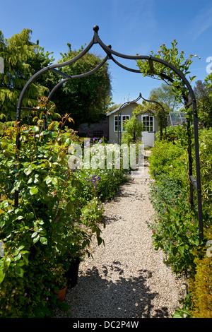Arco di metallo che conduce su un sentiero di ghiaia a fiore boarder e summerhouse sul giardino inglese, Inghilterra Foto Stock