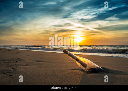 Un messaggio in bottiglia su una spiaggia contro il sole di setting Foto Stock