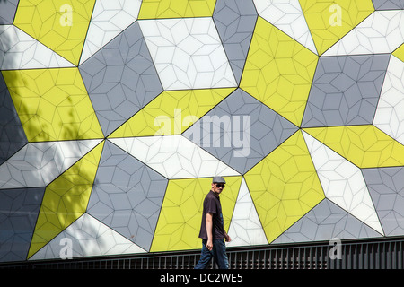 Uomo che indossa il tappo piatto e occhiali da sole a piedi passato variopinto mosaico a parete Foto Stock