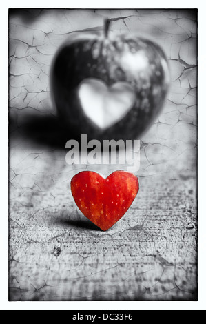 Una mela rossa con una forma di cuore cut-out. Una parte è a colori e l'altra parte è in bianco e nero. Rappresentazione di amore.