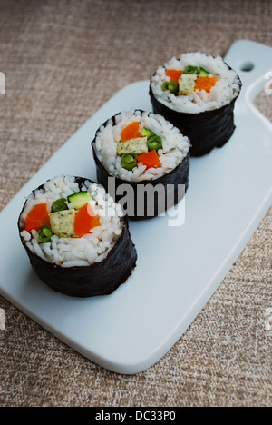 Vegetariano maki sushi rotoli con riso, carote, zucchine, fagioli verdi, tofu e nori alghe nel piatto bianco su sfondo naturale Foto Stock