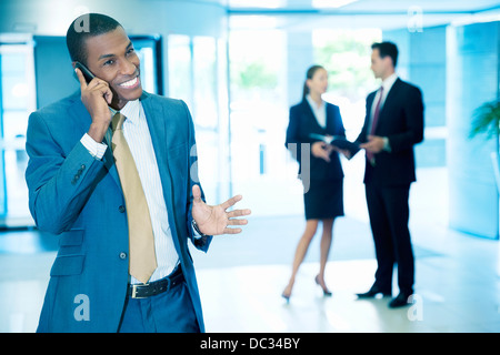 Imprenditore sorridente parlando al cellulare e gesticolando nella lobby Foto Stock