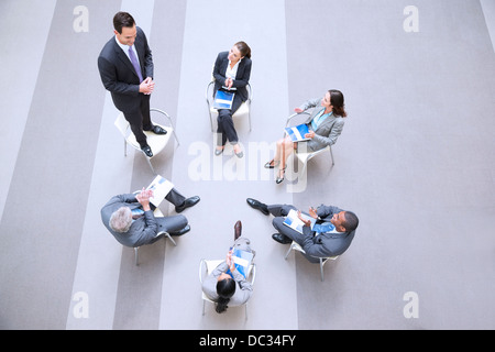 Elevato angolo di visione di imprenditore in piedi su una sedia in cerchio con co-lavoratori Foto Stock