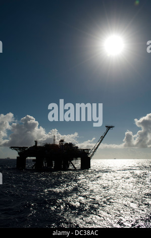 Silhouette di un impianto di trivellazione petrolifera nella zona offshore, disco indietro luce, cielo blu, refelection sulla superficie dell'acqua. Foto Stock