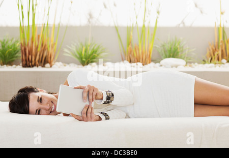 Ritratto di donna sorridente posa sul divano del patio con tavoletta digitale Foto Stock