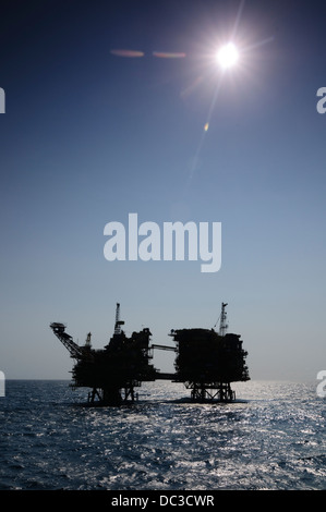 Silhouette di un impianto di trivellazione petrolifera nella zona offshore, disco indietro luce, cielo blu, refelection sulla superficie dell'acqua. Foto Stock