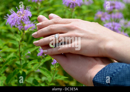 Appena fidanzati mostrare l'anello di fidanzamento in un giardino con fiori in background Foto Stock