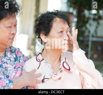 Tristezza senior donna asciugare le lacrime negli occhi e consolante da sua figlia maturo, naturale parco all'aperto. Foto Stock