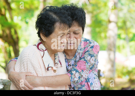 Candide colpo di un asiatico donna matura abbracci e consolante il suo pianto vecchia madre all'aperto parco naturale. Foto Stock