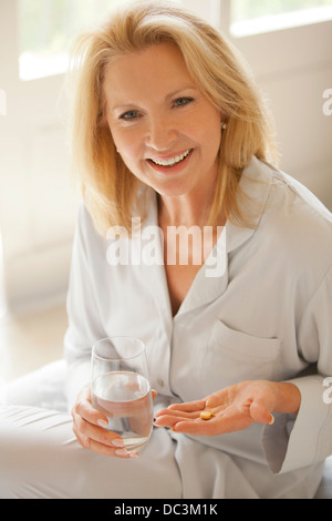 Ritratto di donna sorridente holding pillola e bicchiere di acqua Foto Stock