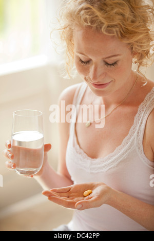 Donna che mantiene un bicchiere di acqua e pillole Foto Stock