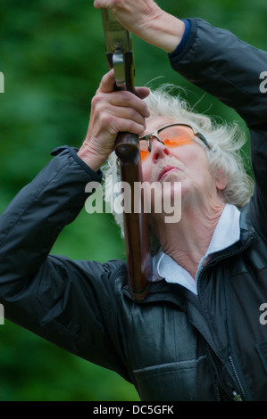 Signora sparare con un fucile da caccia a un gioco di simulazione di tiro al piattello giorno Foto Stock