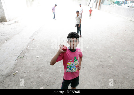 Un giovane ragazzo indiano si mette in mostra la sua sfera di cricket durante una partita di cricket di strada a Delhi. Foto Stock