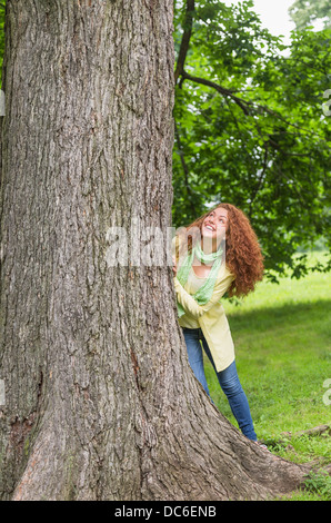 Donna appoggiata su albero in posizione di parcheggio Foto Stock