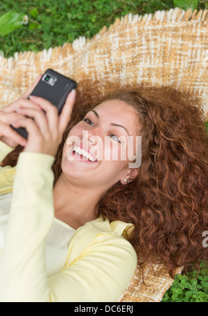 Donna sdraiata su erba nel parco e utilizzando il telefono cellulare Foto Stock