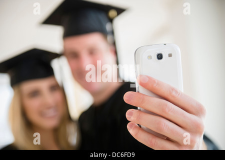 Coppia di amici in abiti di graduazione di prendere foto con lo smartphone Foto Stock