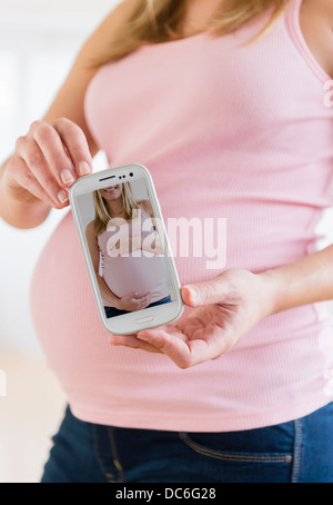 La sezione centrale della donna incinta tenendo il telefono cellulare Foto Stock