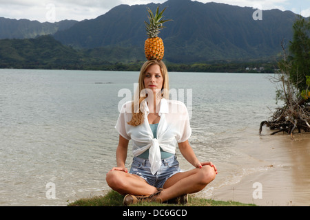 Una giovane donna caucasica medita con un bilanciamento di ananas sulla cima della sua testa in Honolulu, Hawaii. Foto Stock