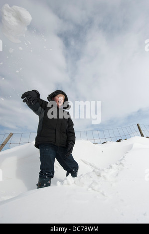 Ragazzo gettando grande palla di neve e divertimento nella neve. Cumbria, Regno Unito Foto Stock