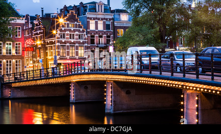 Ponte Halvemaans da Amsterdam, illuminato, con tipiche case olandesi in background Foto Stock