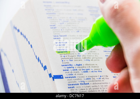 Close-up di un uomo le mani usando una sostanza fluorescente marcatore verde per evidenziare la parola da cercare su un dizionario Foto Stock