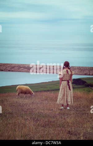 Una ragazza in un abito vintage su un prato con una pecora Foto Stock