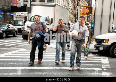 3 buon natured di lavoratori edili in luoghi polverosi stivali da lavoro & portando gli elmetti cross Broadway dopo il lavoro nel centro di Manhattan Foto Stock