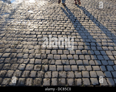 Le ombre e i piedi delle persone che camminano sul sentiero acciottolato accanto al Fiume Tamigi a Richmond, Londra Foto Stock