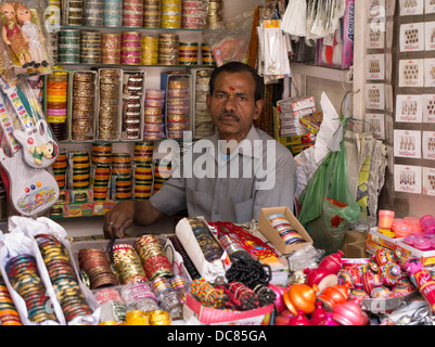 Proprietario del negozio con tilak rosso sul fronte vendendo schiave in Varanasi India Foto Stock