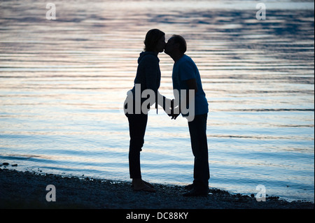 Un giovane è il bacio al tramonto sulla spiaggia di un lago Foto Stock