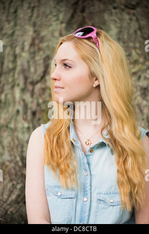 Una bionda e giovane donna attraente di fronte di alberi in un parco Foto Stock