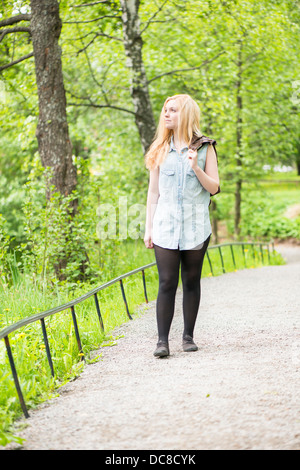 La natura in scena con una giovane donna attraente appoggiata contro un albero in un parco Foto Stock