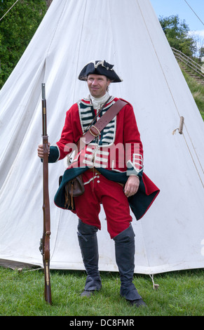 Un soldato di cappotto rosso del 18C nell'esercito britannico, che tiene Brown Bess Musket, in piedi come guardia contro la tenda bianca all'evento di re-enactment, il castello di Tutbury, Regno Unito Foto Stock