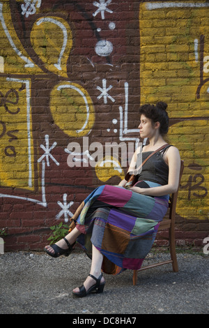 Giovane donna si siede di fronte al fresco parete dipinta sul lato di Kensington maneggio, Brooklyn, New York. Foto Stock
