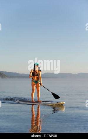 Una donna, Stand Up Paddleboarding (SUP) sul Lago Tahoe al mattino presto sulle calme acque vetroso, CA. Foto Stock