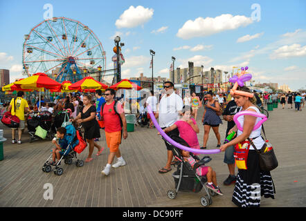 Brooklyn, New York, Stati Uniti d'America. Il 10 agosto 2013. A Coney Island boardwalk, IVELIZ BALTAZAR da Harrison, New Jersey, indossa un palloncino colorato cappello e grembiule, come ella crea forme a palloncino per un giovane bambino, con il parco dei divertimenti di Wonder Wheel in background. Foto Stock